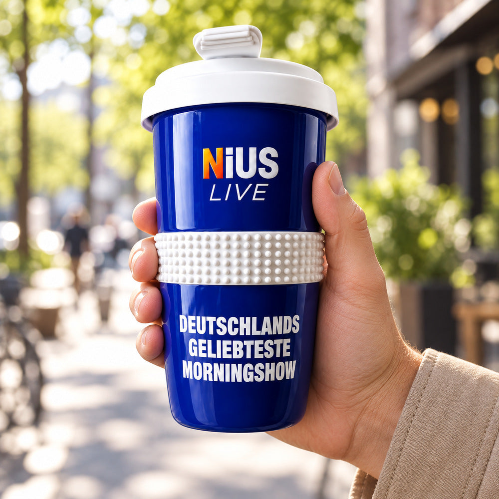 Hand hält den blauen NIUS LIVE Coffee-to-Go-Becher mit Silikonbanderole auf einer sonnigen Straße